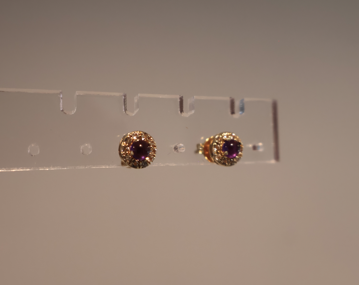 Pair of gold earrings with purple gemstones on a clear stand against a plain background