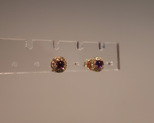 Pair of gold earrings with purple gemstones on a clear stand against a plain background
