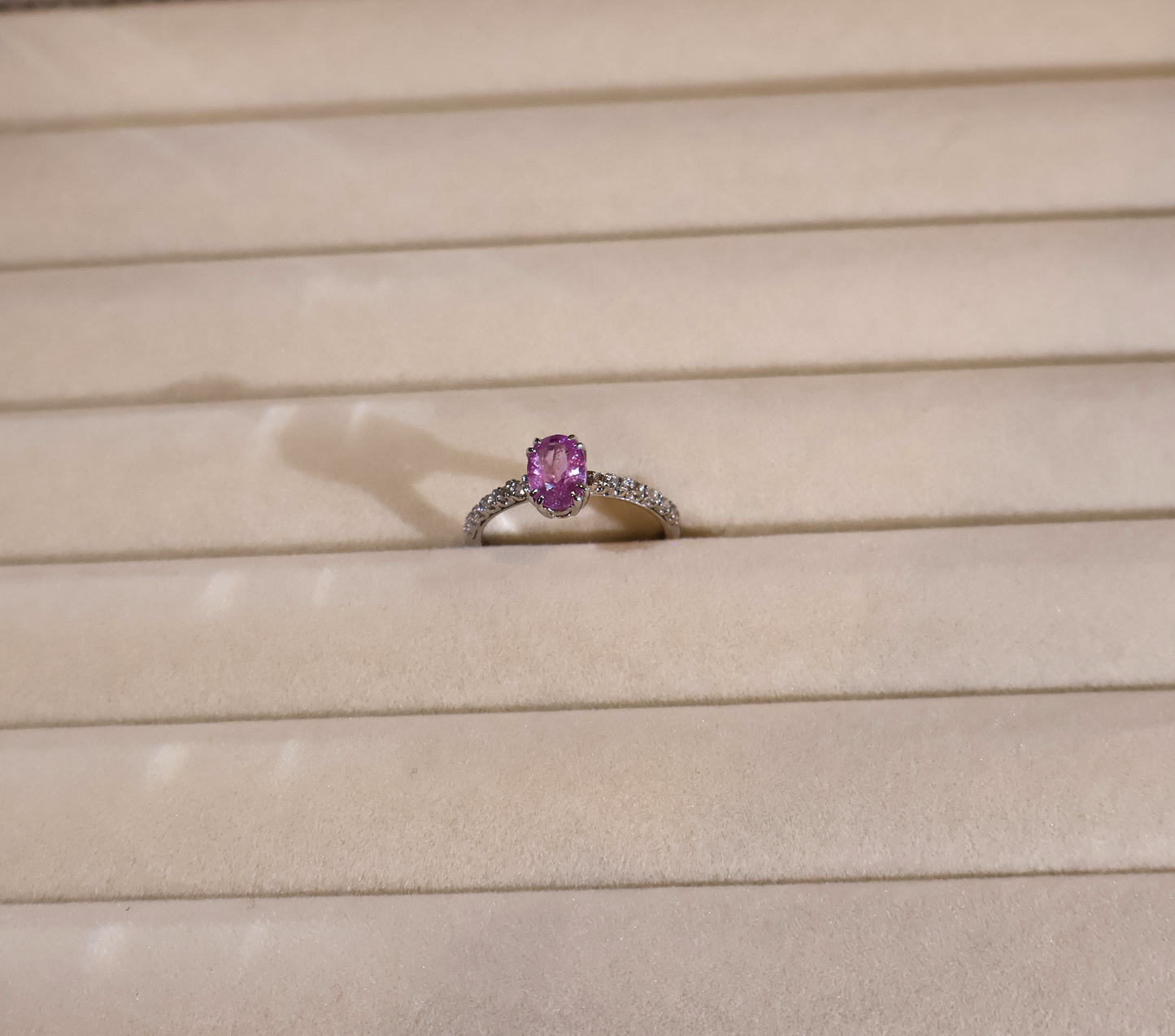 White gold ring with a pink sapphire on a beige surface