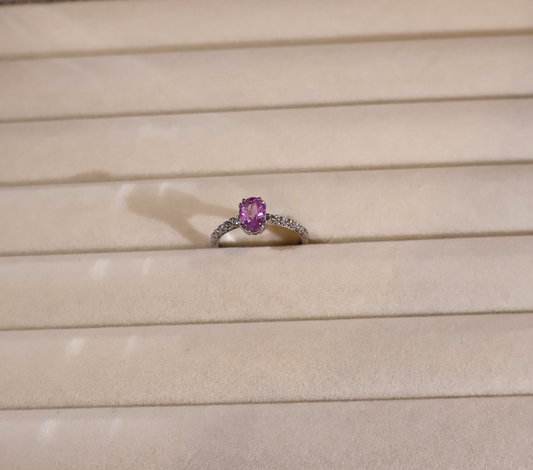 White gold ring with a pink sapphire on a beige surface