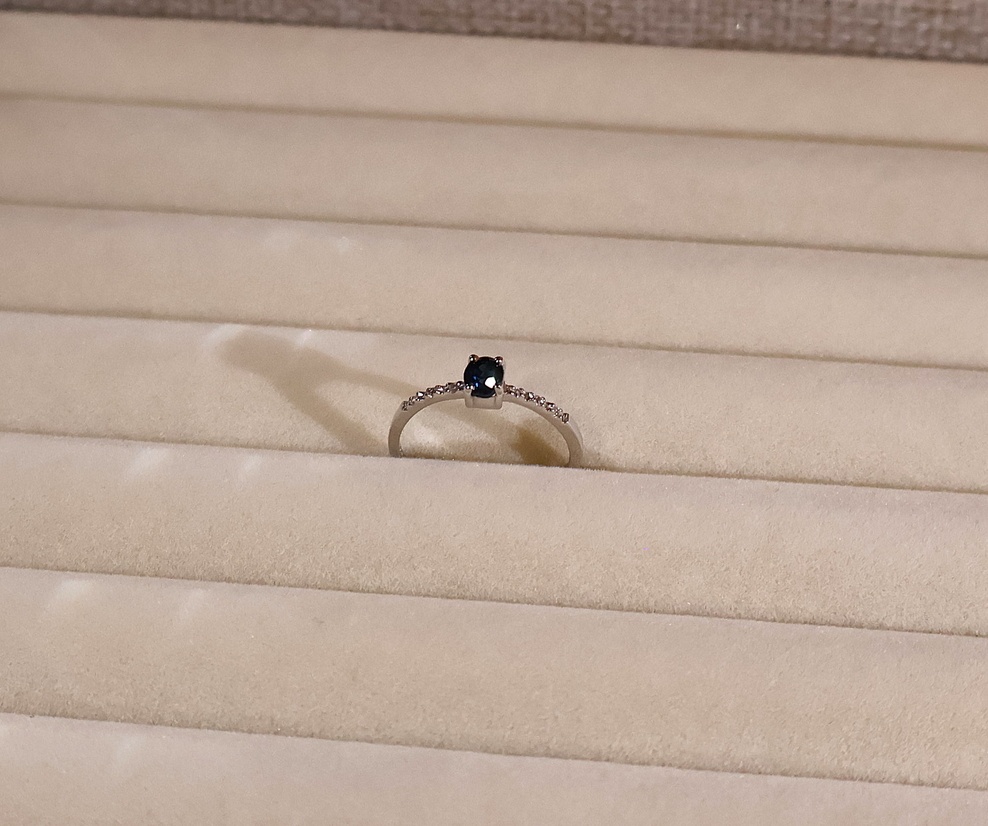 White gold ring with a blue sapphire gemstone on a beige fabric background