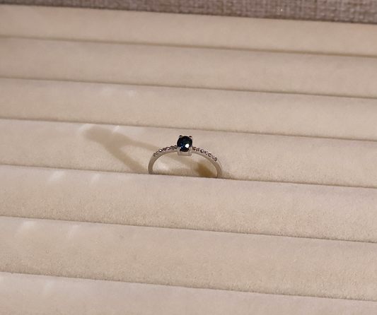 White gold ring with a blue sapphire gemstone on a beige fabric background