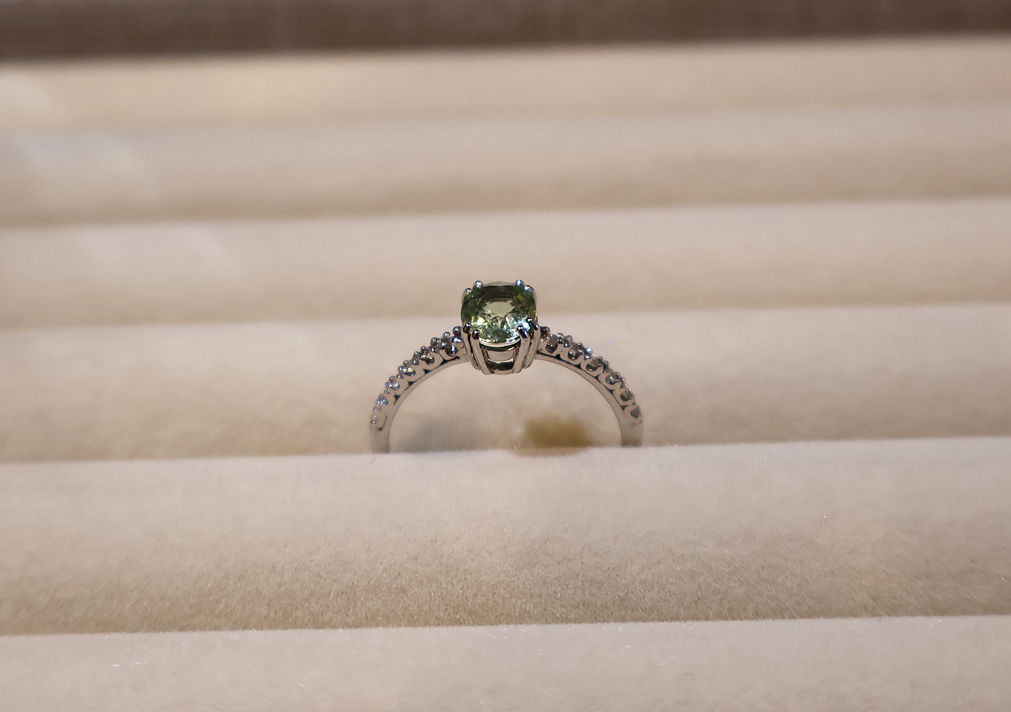 White gold ring with a green gemstone peridot on a beige cushion