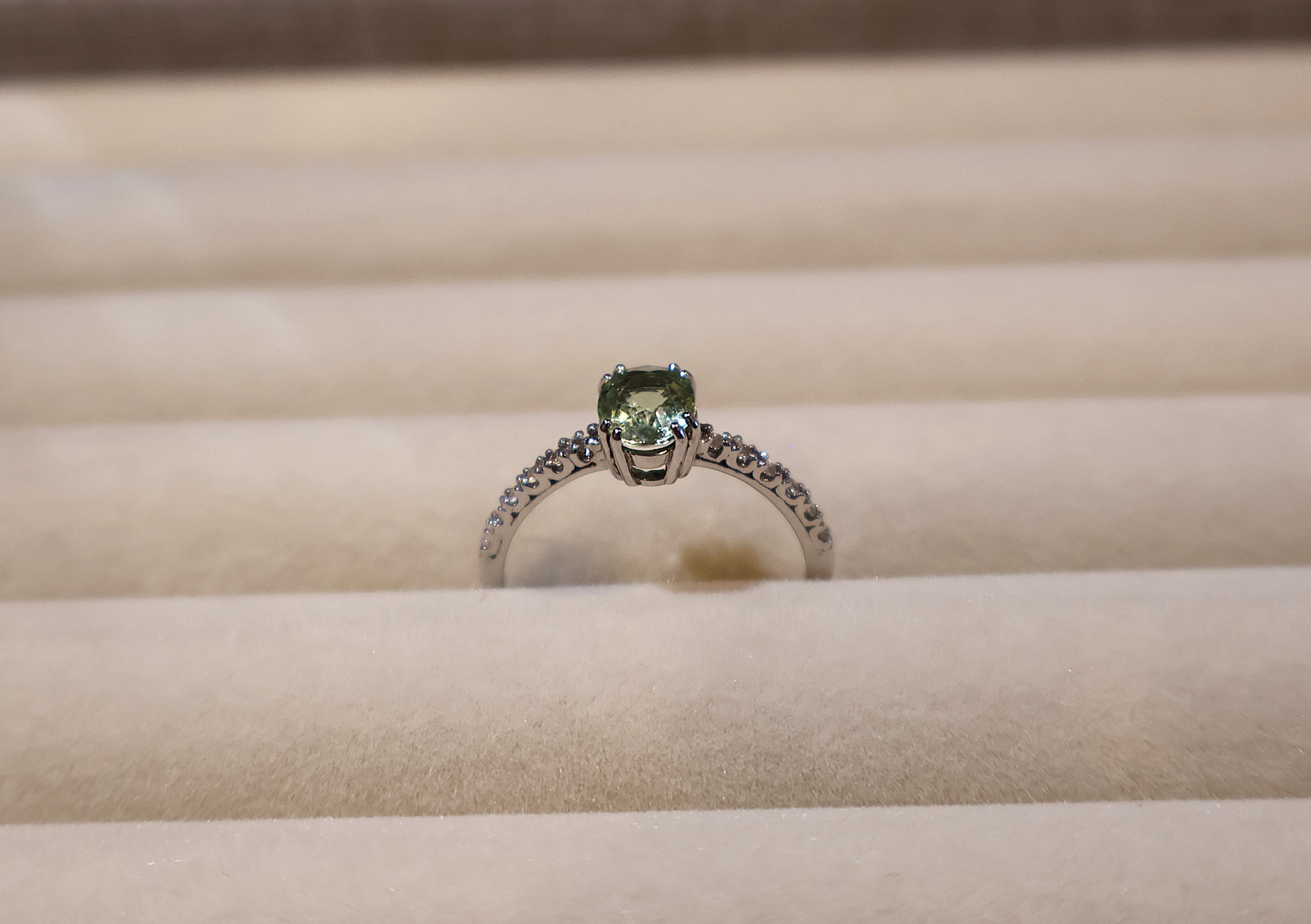 White gold ring with a green gemstone peridot on a beige cushion